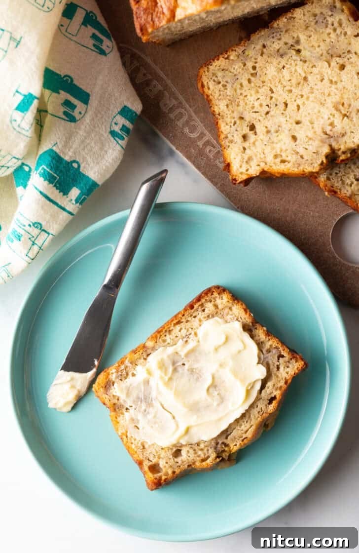 A delicious slice of 4-ingredient banana bread, generously spread with butter, resting on a charming blue plate beside a knife.