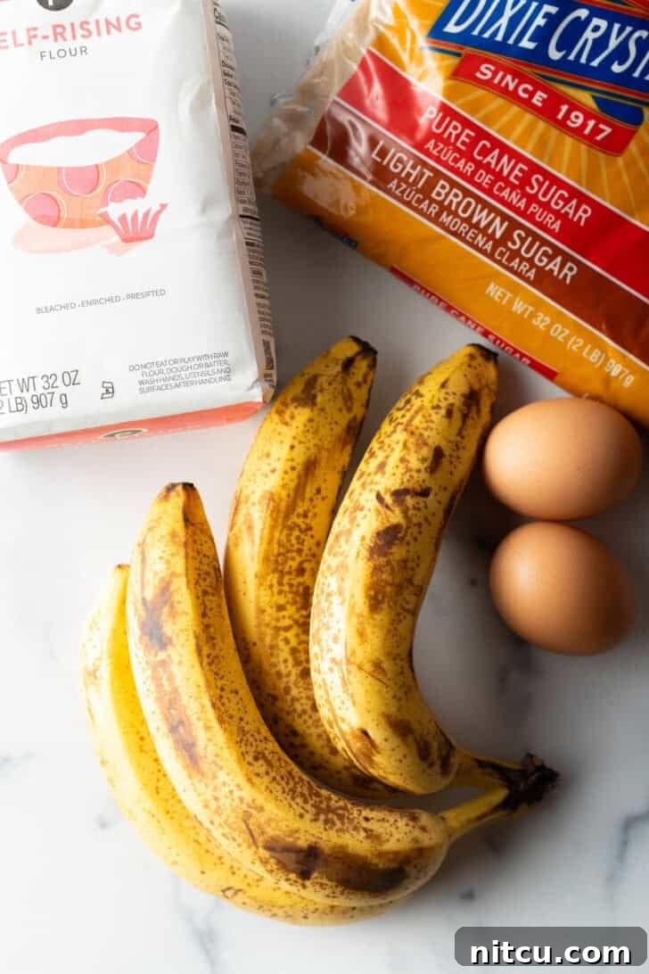 Top-down view of all the essential recipe ingredients: a bunch of perfectly ripe bananas, a bag of self-rising flour, a bowl of light brown sugar, and two fresh eggs.