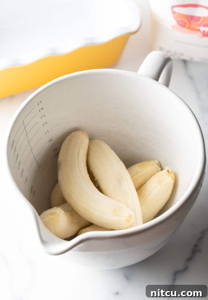 Five peeled ripe bananas in a large white mixing bowl, ready to be mashed.