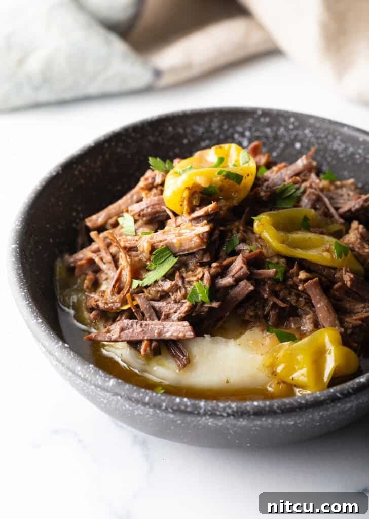 Black bowl with a layer of mashed potatoes topped with shredded pot roast and pepperoncinis.
