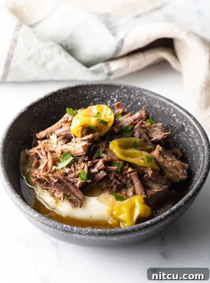 Black bowl with a layer of mashed potatoes topped with shredded pot roast and pepperoncinis.