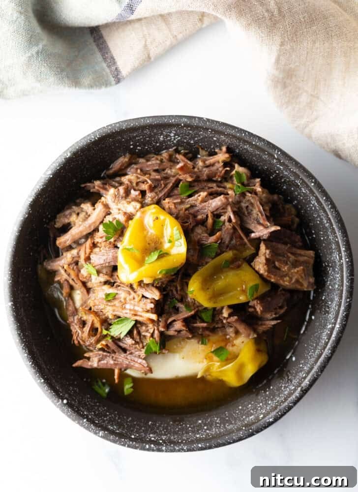 Top down view of a black bowl with a layer of mashed potatoes topped with shredded pot roast and pepperoncinis.