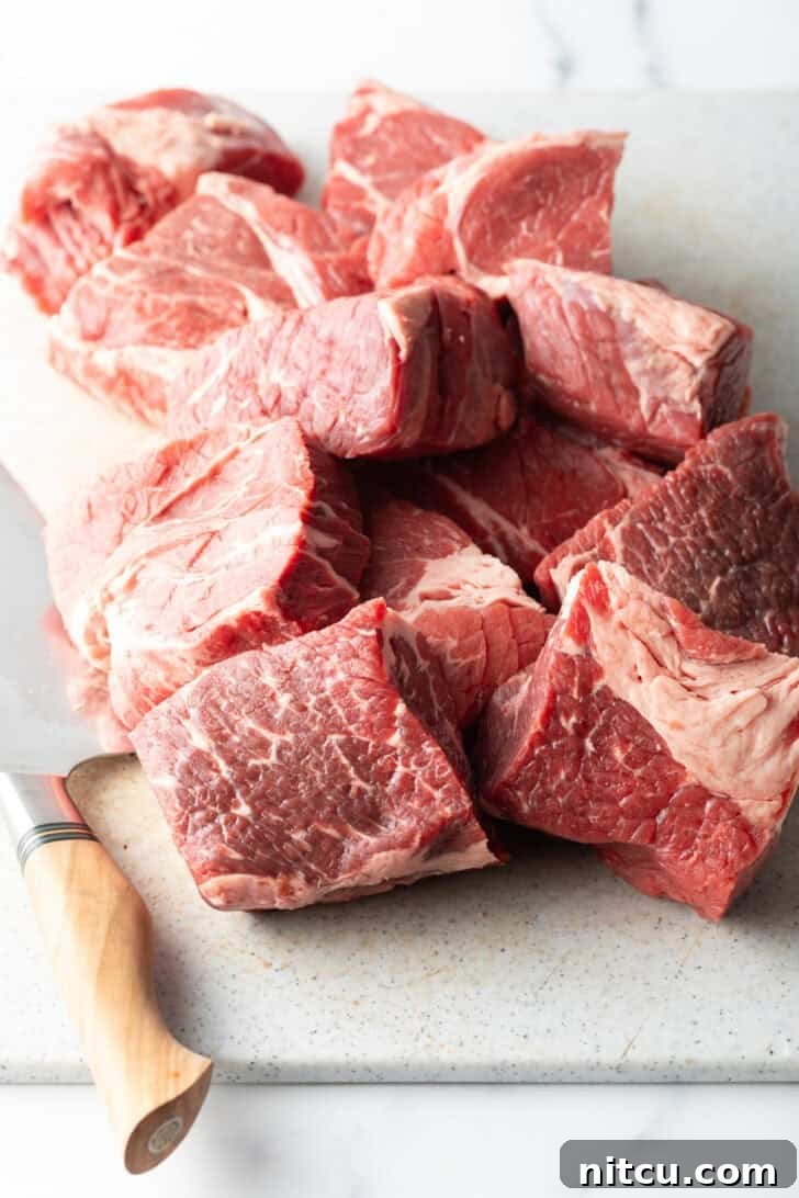 Chunks of raw meat on a cutting board with sharp knife.