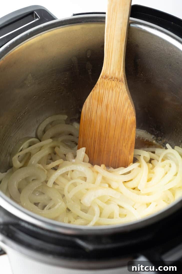 Using a wooden spatula to saute onion slices in an instant pot.