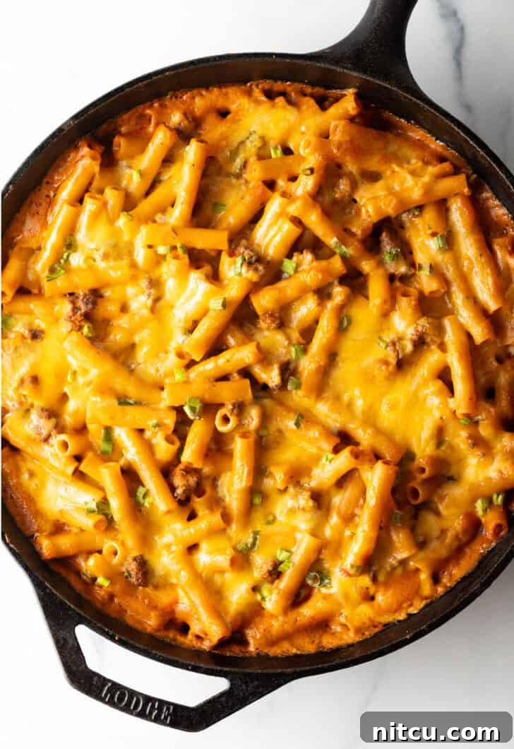 Top deep black cast iron skillet with long noodles, ground beef, and cheese. A perfectly cooked and bubbling cheeseburger casserole, ready to serve.