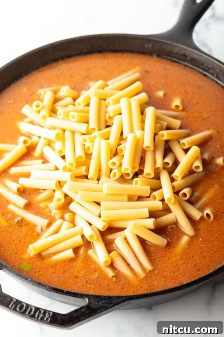 Adding long pasta noodles to a skillet with ground beef and tomato sauce. The pasta is raw and will cook directly in the sauce.