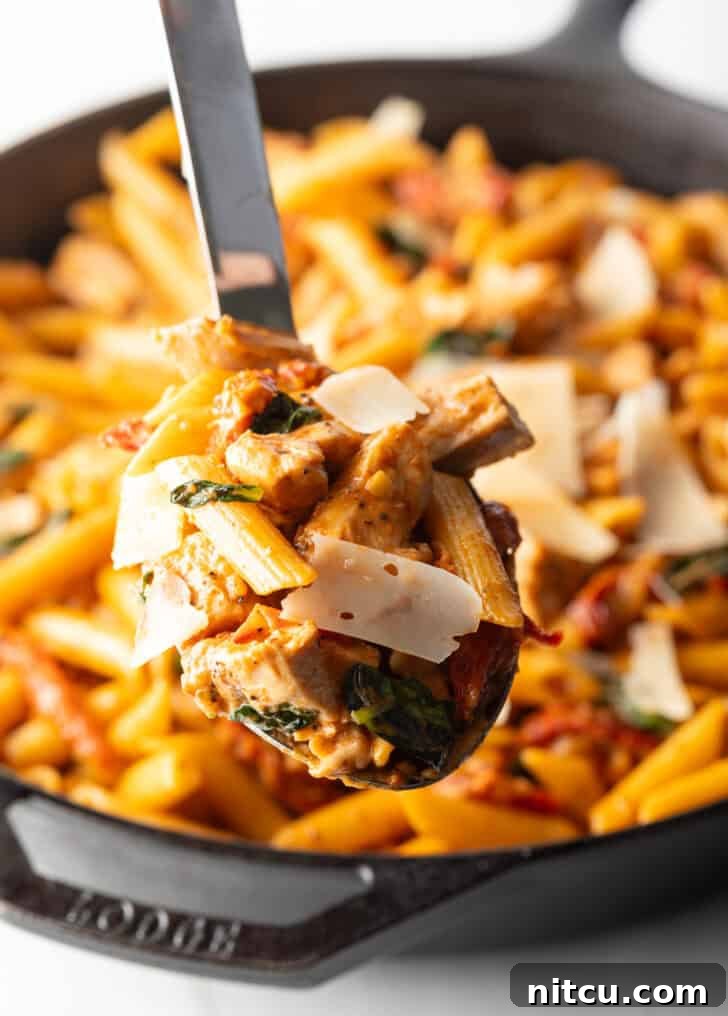 A large spoonful of spicy Marry Me Chicken Pasta, held up to the camera, showcasing creamy sauce, chicken pieces, and sun-dried tomatoes.
