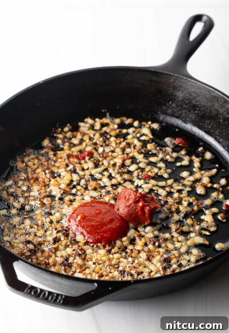 Sautéing minced garlic and rich tomato paste in a cast iron skillet, building the flavor base.