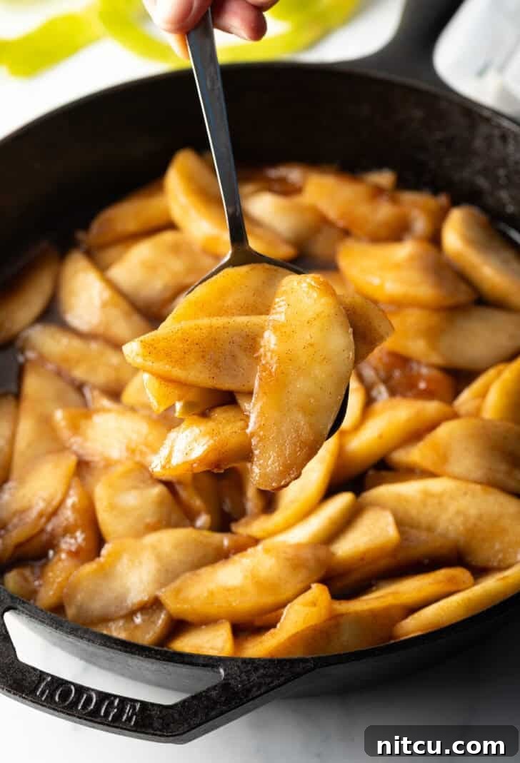 A spoon lifting a serving of glistening spiced apple slices, showcasing their tender texture.