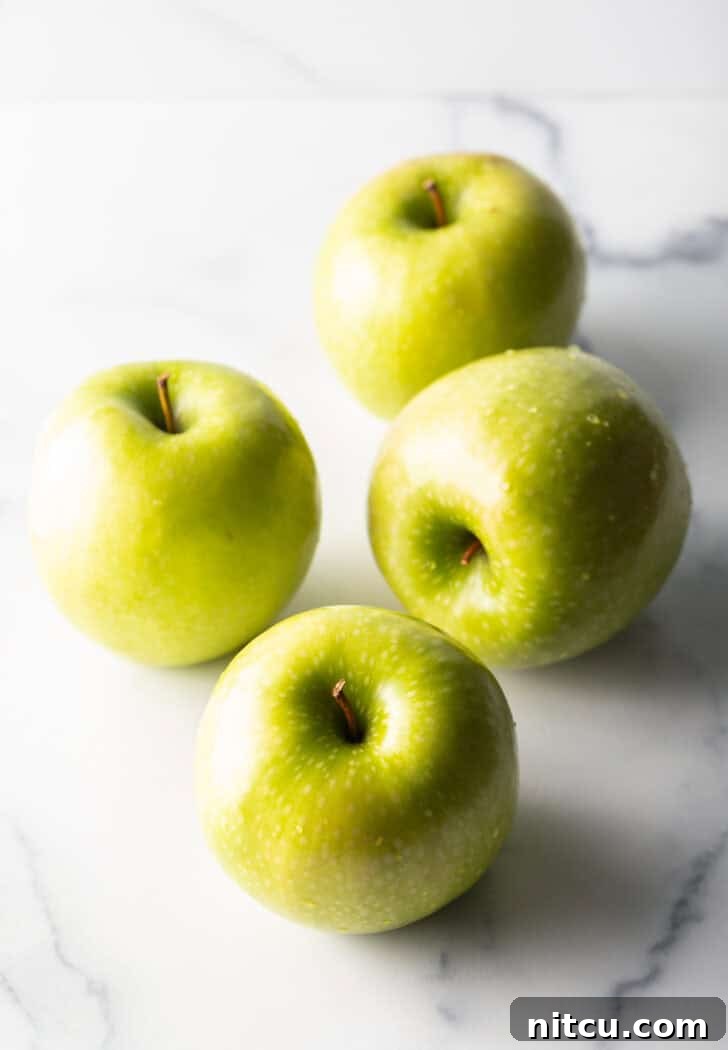 Four whole Granny Smith apples, fresh and ready for preparation.