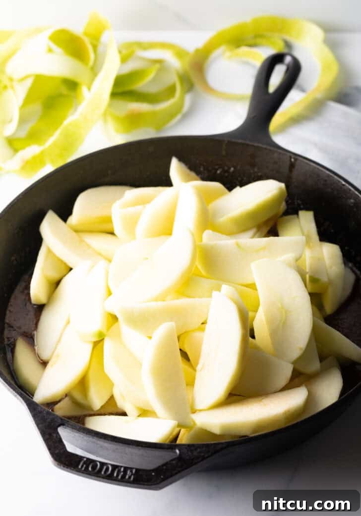 A mounded pile of raw apple slices in a cast iron skillet, ready to be fried.