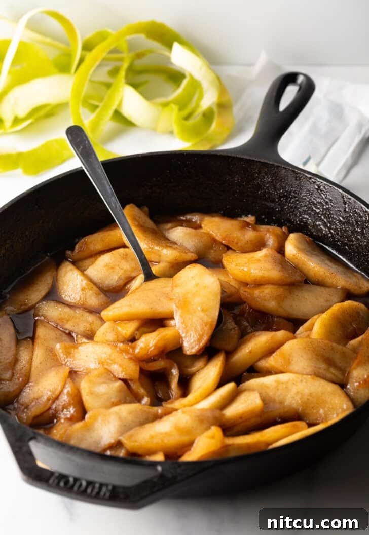 A spoon gently stirring the apple slices in the skillet as they cook, ensuring even coating.