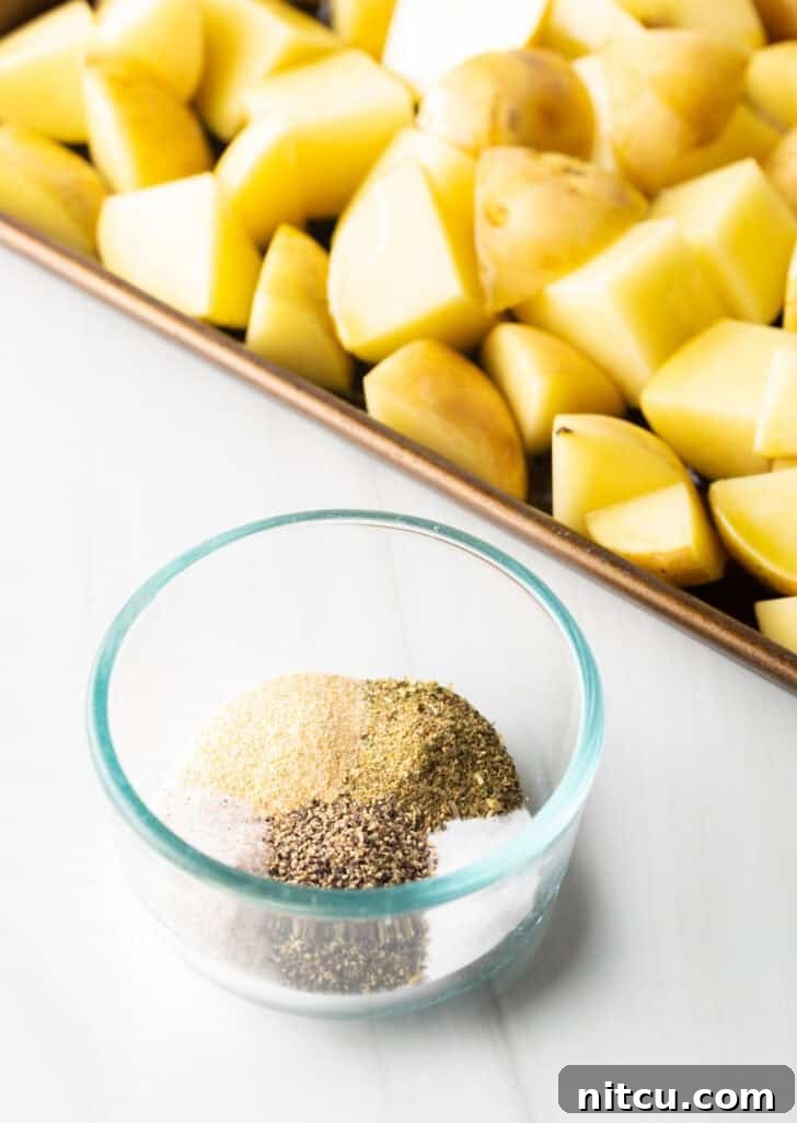 Raw pieces of yukon potatoes on a baking sheet, with a glass dish on the side filled with assorted spices.
