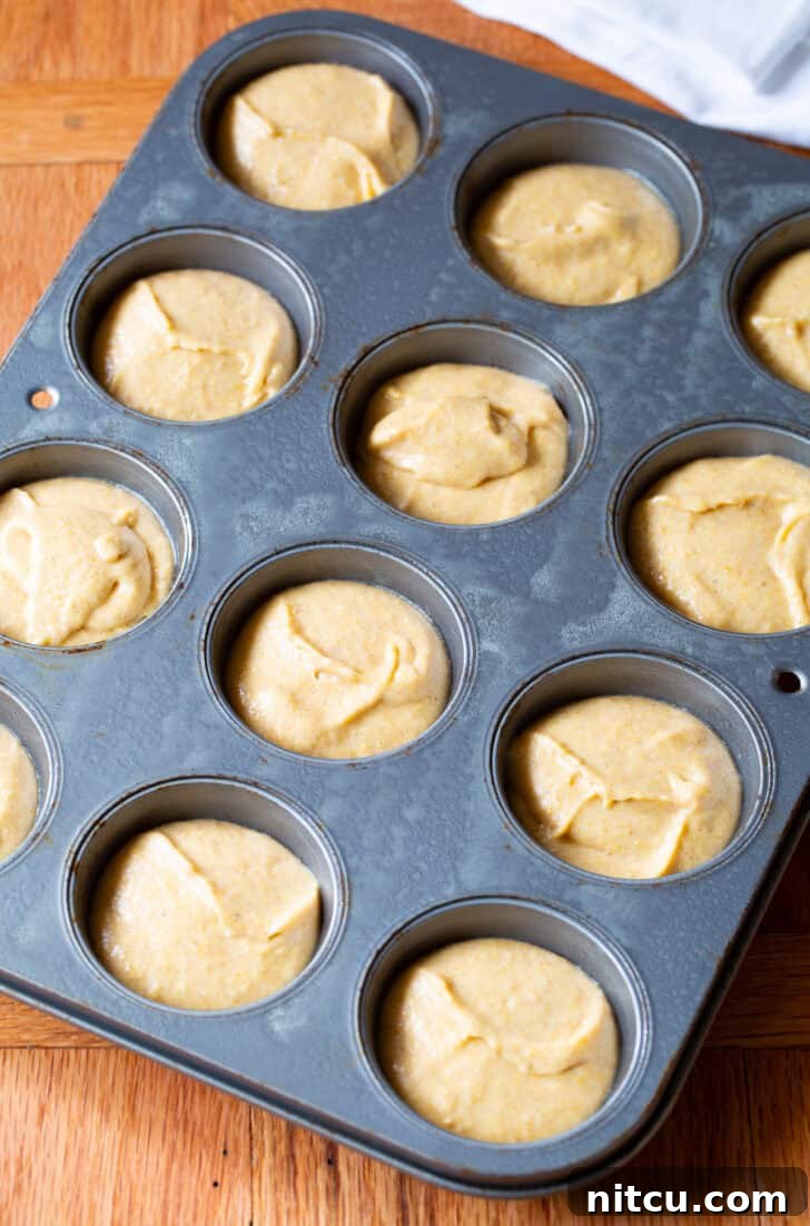 Smooth, golden corn muffin batter evenly distributed into a 12-cup baking tin, ready to be baked into delicious muffins.