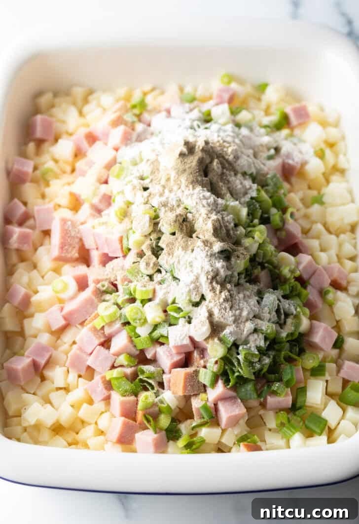 Mixing potatoes, ham, green onions, and garlic in a baking dish.