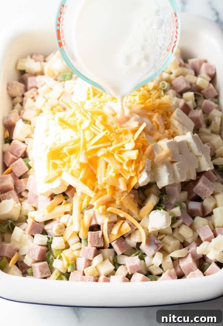 Adding milk to the chopped potatoes, ham, and shredded cheese in a casserole dish before baking.