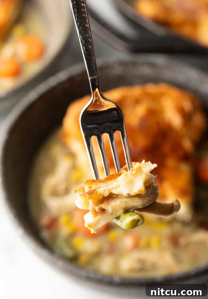 Fork holding a bite of chicken pot pie to camera, showing the creamy filling and flaky crust.