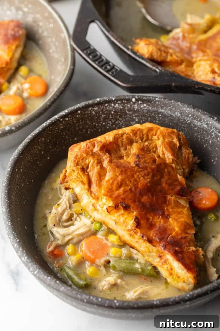 A top-down view of a wedge of golden puff pastry chicken pot pie on a black plate, ready to be enjoyed.