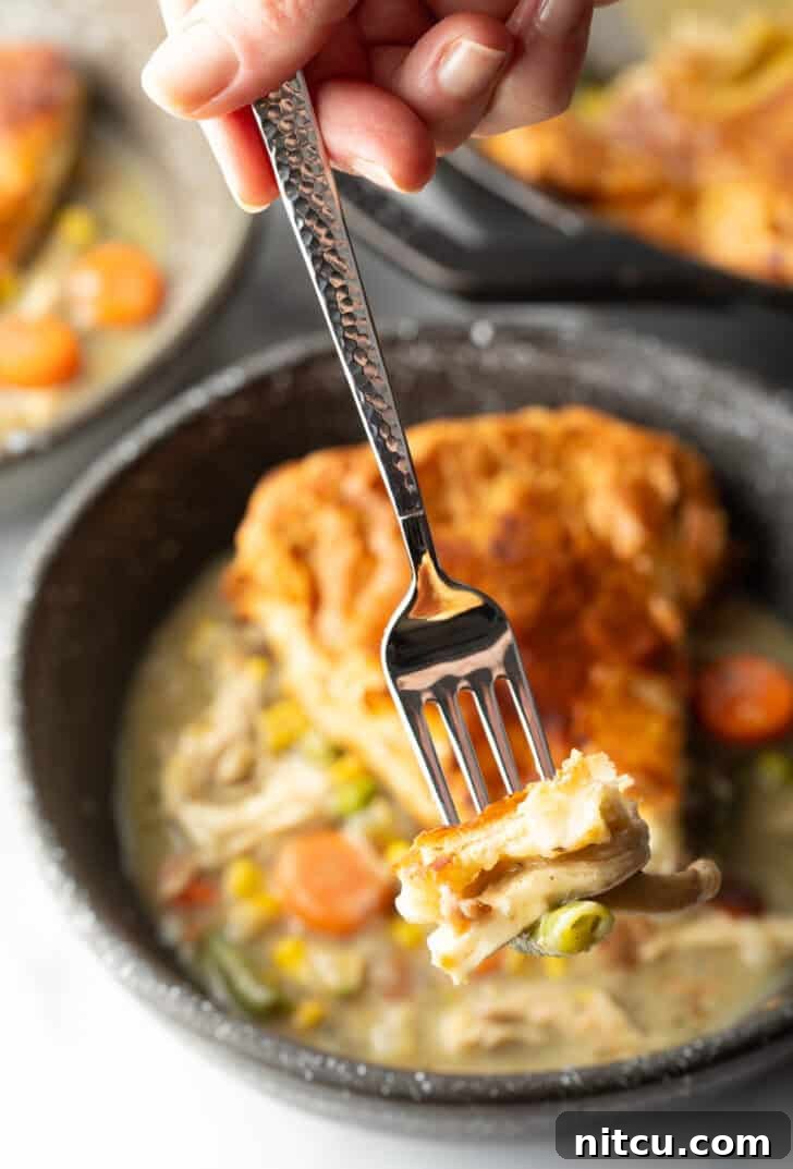 A fork holding a bite of creamy chicken pot pie with puff pastry crust, ready to eat.