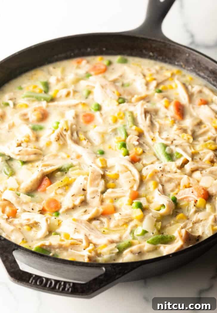A cast iron skillet filled with creamy chicken and vegetables, ready for the puff pastry topping.