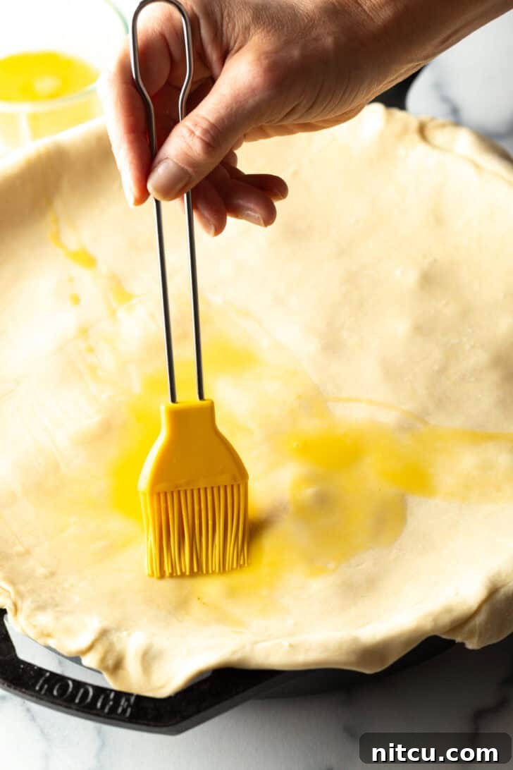 A hand using a yellow pastry brush to evenly coat the top of puff pastry with an egg wash.