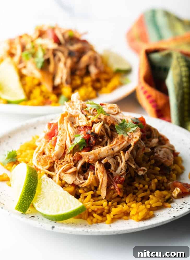 Mound of zesty shredded Mexican chicken on a plate with spanish rice and lime wedges.