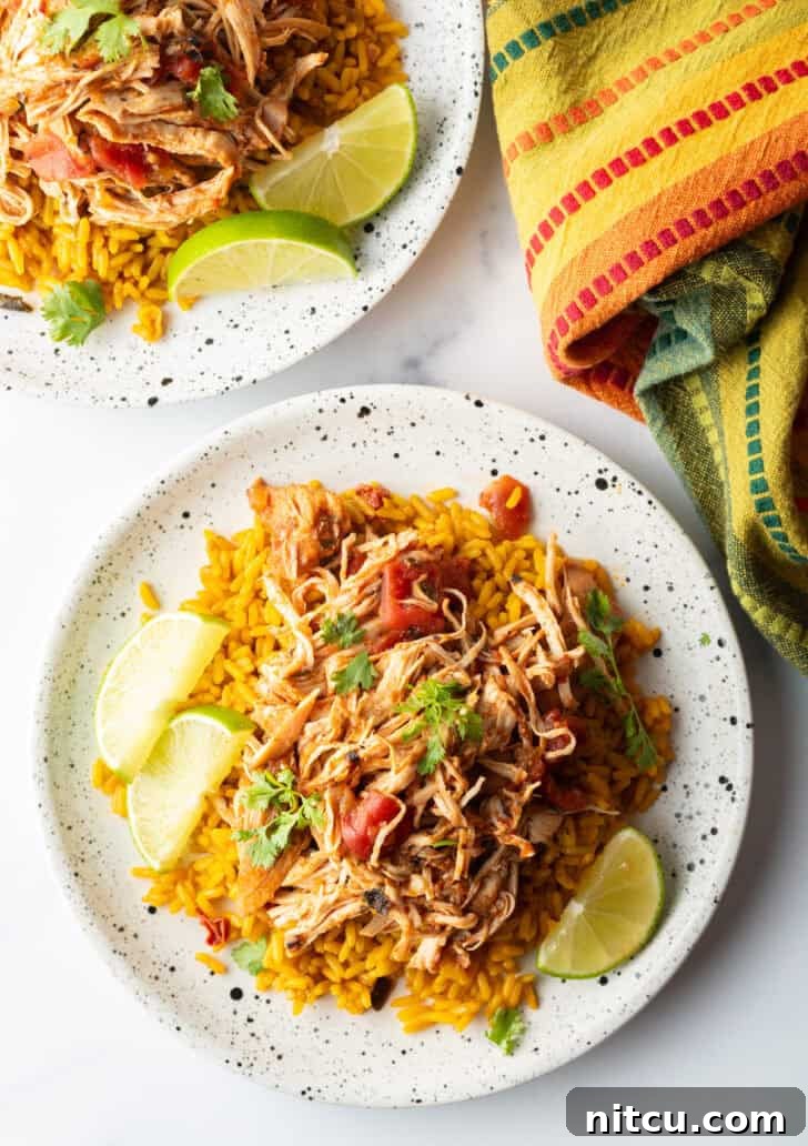 Top down view mound of zesty shredded Mexican chicken on a plate with spanish rice and lime wedges.