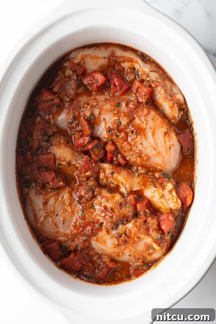 Several whole chicken breasts covered in red sauce in a white crockpot.