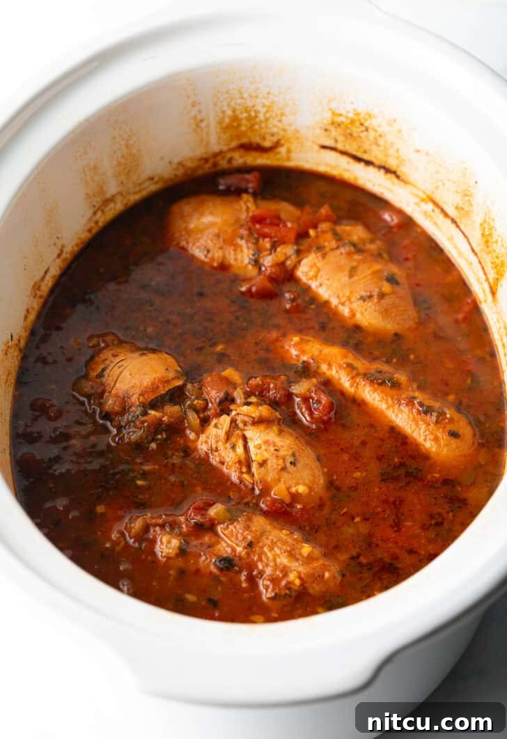 Several whole chicken breasts covered in red sauce in a white crockpot.