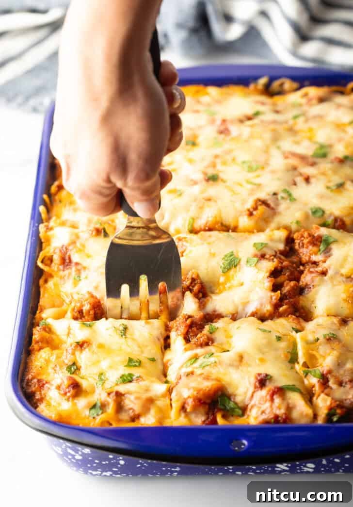 Using a metal spatula to cut the cheesy spaghetti casserole into 12 even pieces for serving.