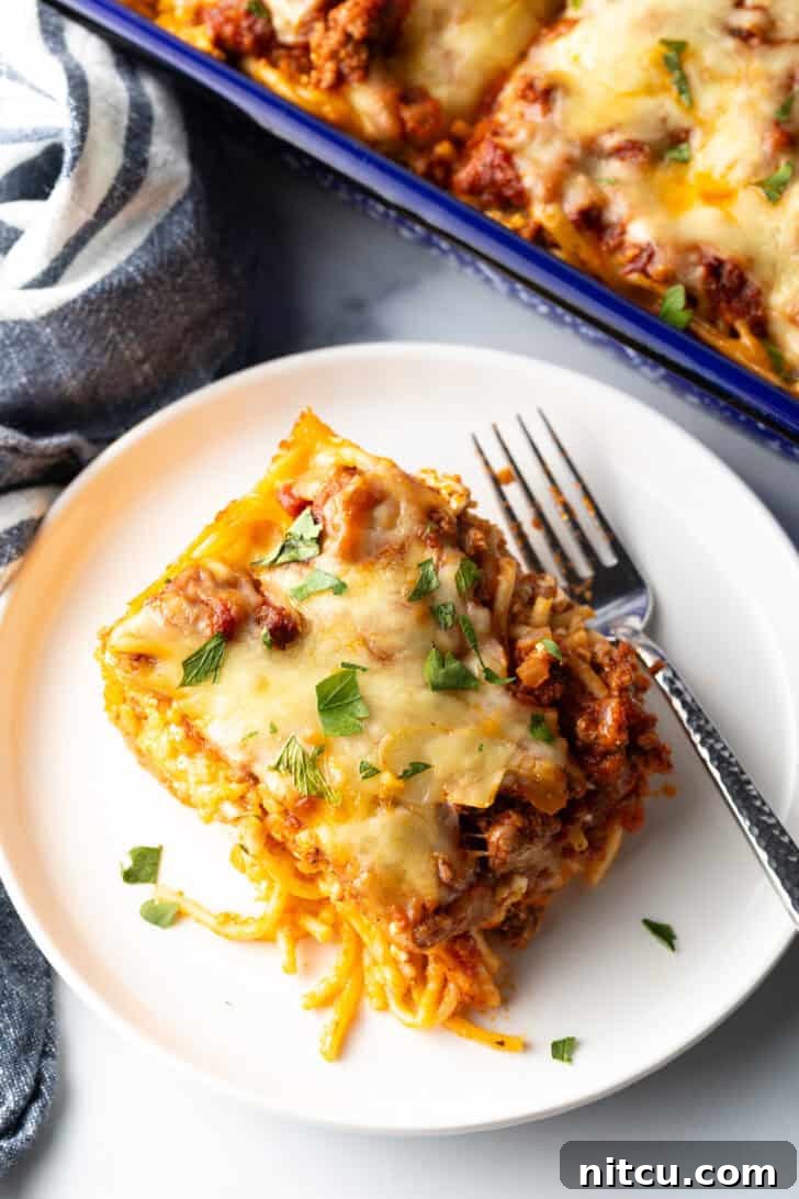 Top down view of a white plate with a single serving of spaghetti bake casserole and a fork, highlighting the cheesy topping.