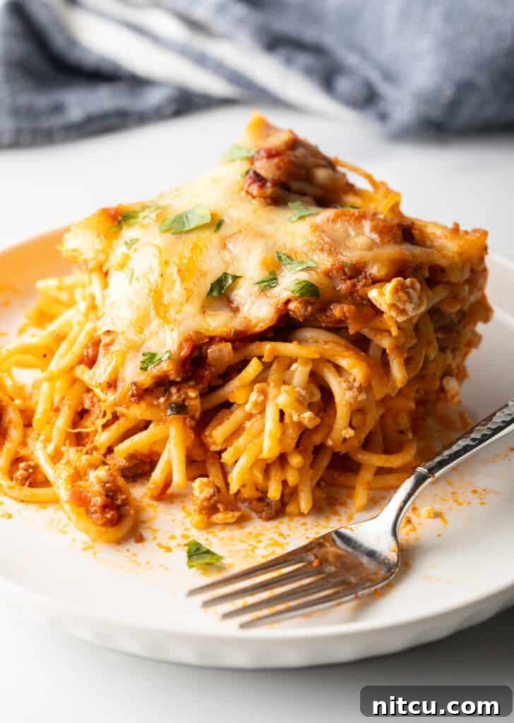 White plate with a generous serving of spaghetti bake casserole and a fork, close-up showing texture and cheese.