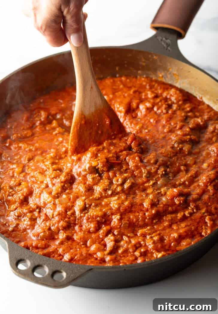 Stirring the meat pasta sauce in a skillet with a wooden spatula to combine flavors.