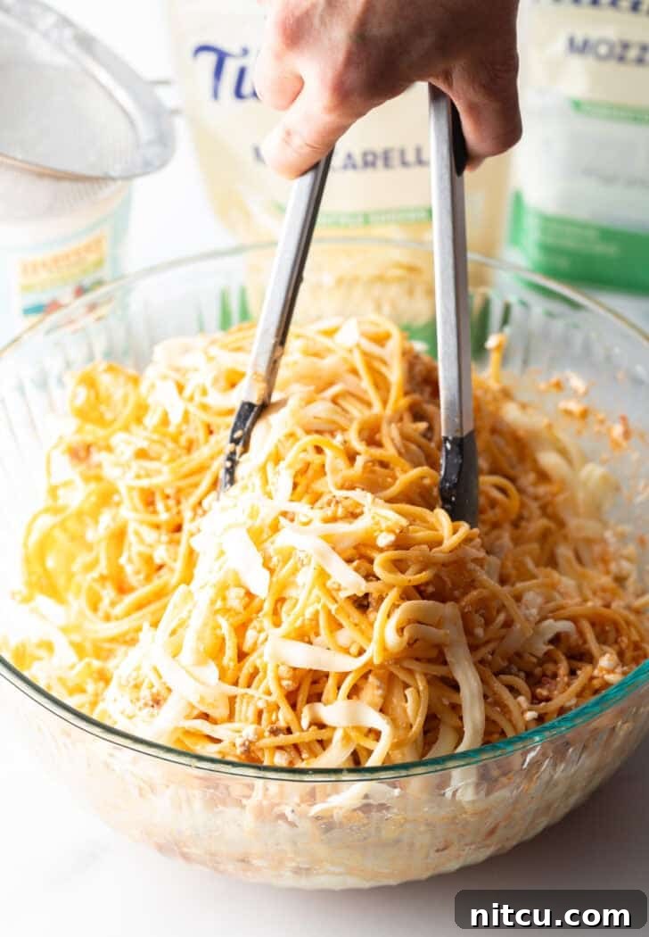 Using tongs to gently toss cooked spaghetti with the cottage cheese mixture in a glass bowl.