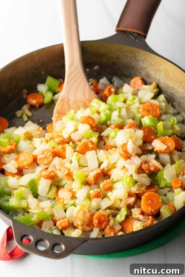 Chopped carrots, celery, and onion being sautéed in a cast iron skillet, releasing their sweet aromas.