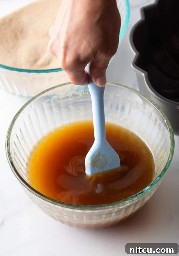 Stirring melted butter, brown sugar, and bourbon with a pastry brush in a glass bowl.