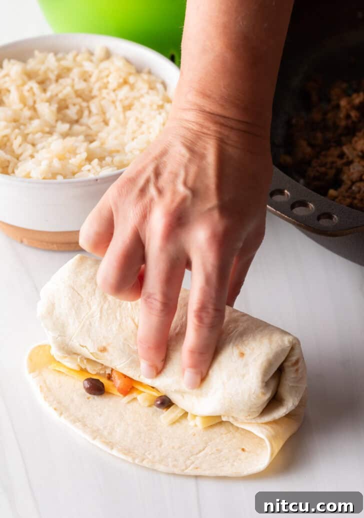 Hand wrapping a beef burrito, demonstrating the careful tuck and roll technique.