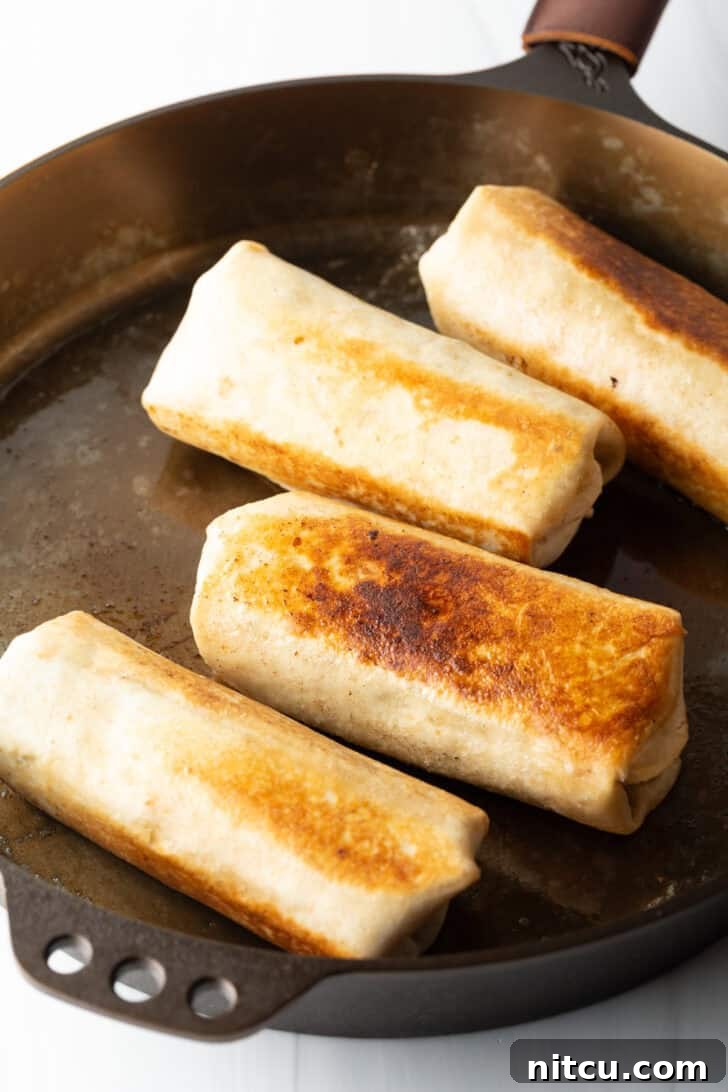 Four beautifully seared burritos on a large pan, golden and ready to serve.