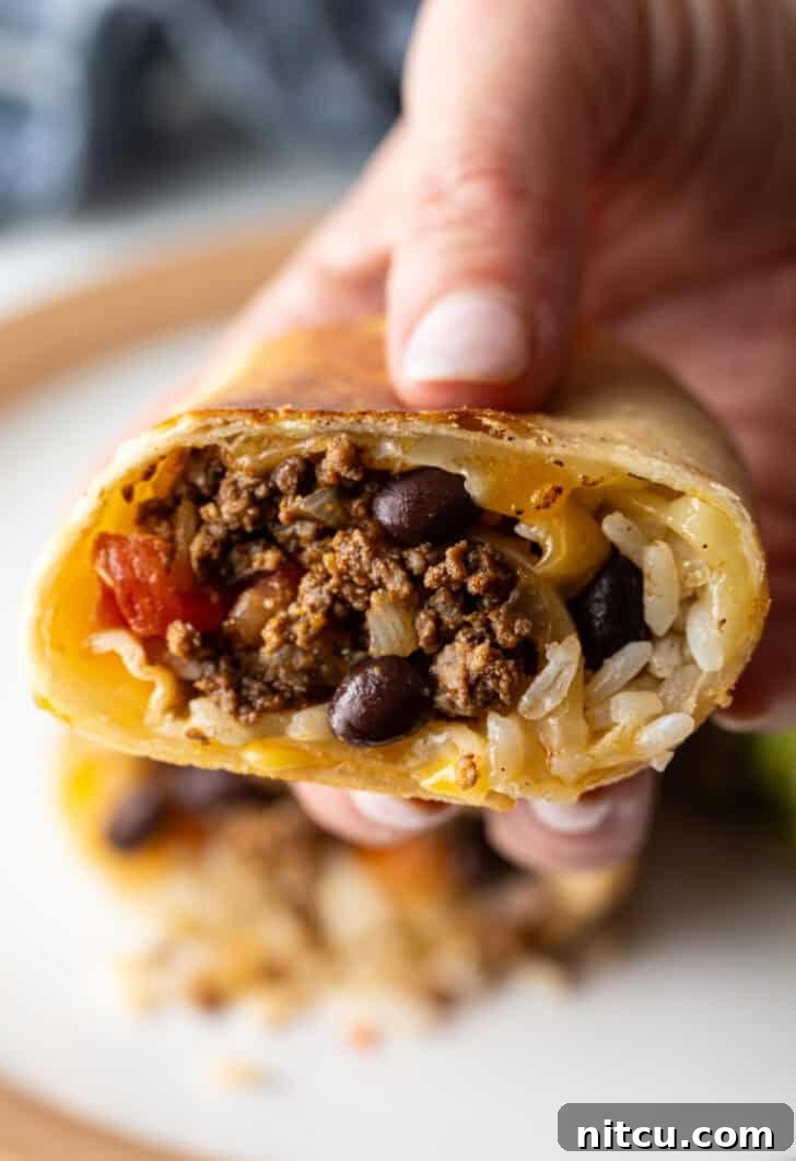 Hand holding the cut side of a beef burrito to camera, showing off the perfectly rolled and delicious interior, ready to be eaten.
