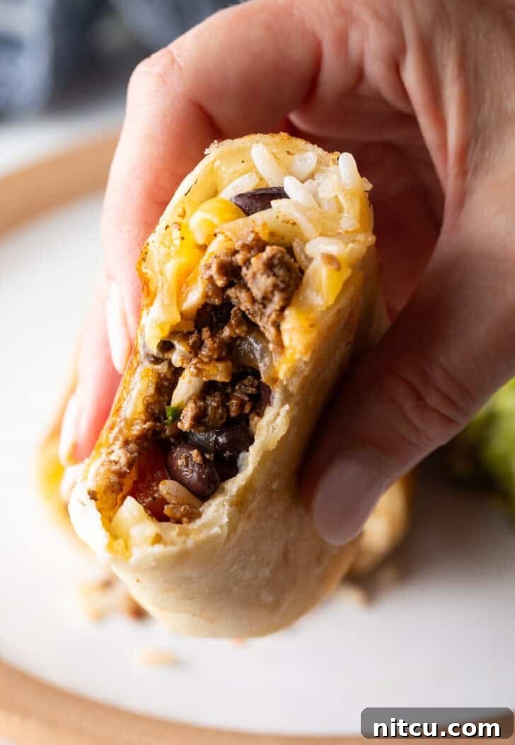 Hand holding the cut side of a beef burrito to camera, showing off the perfectly rolled and delicious interior.