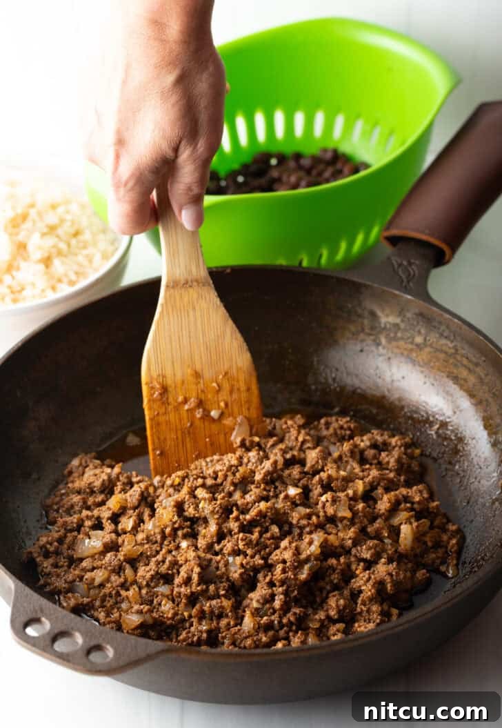 Cooking ground beef in a large skillet with a wooden spoon, the initial step for a flavorful filling.