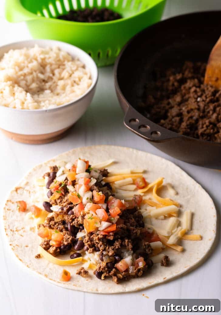 Open-faced flour burrito with shredded cheese, beans, and ground beef, ready for the final touch of pico de gallo.