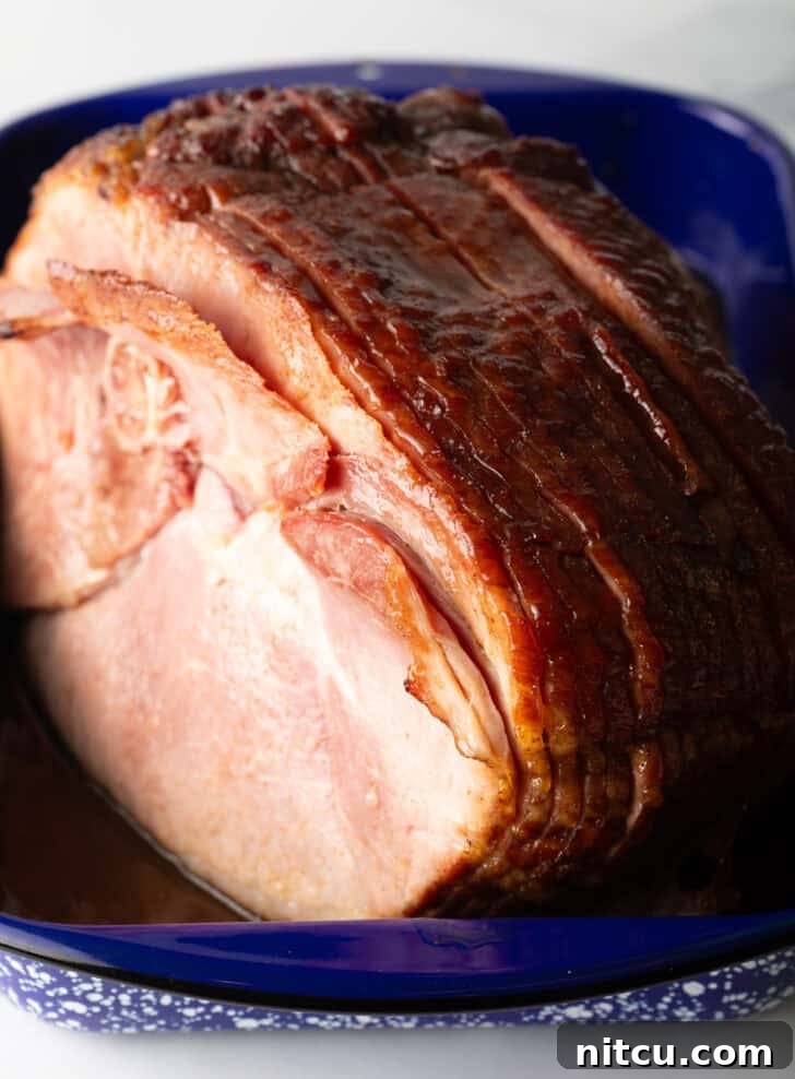 A beautifully cooked spiral ham, glistening with glaze, resting in a blue and white speckled roasting pan, ready to be carved and enjoyed.