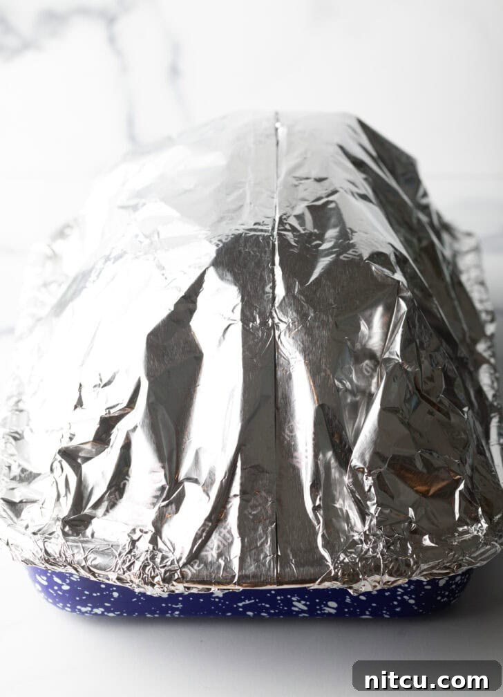 Ham and pan tightly wrapped in aluminum foil, ready for the oven to ensure moisture is retained.