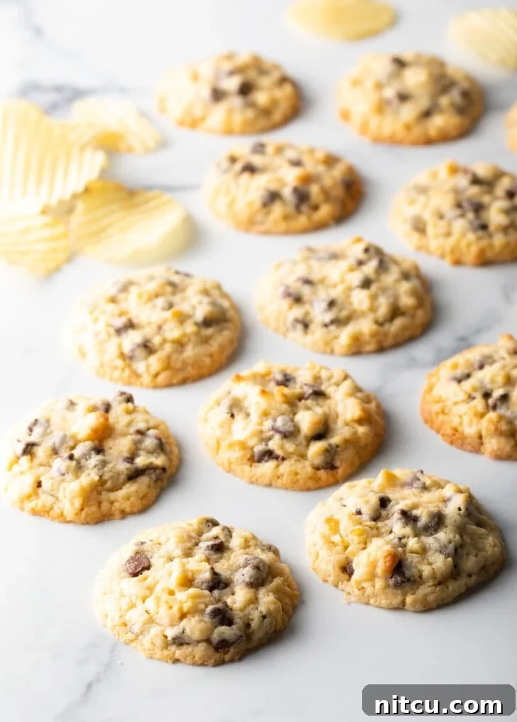Overhead view of perfectly baked potato chip cookies arranged on a marble surface, with scattered potato chips nearby, highlighting their golden-brown edges and chocolate pools.