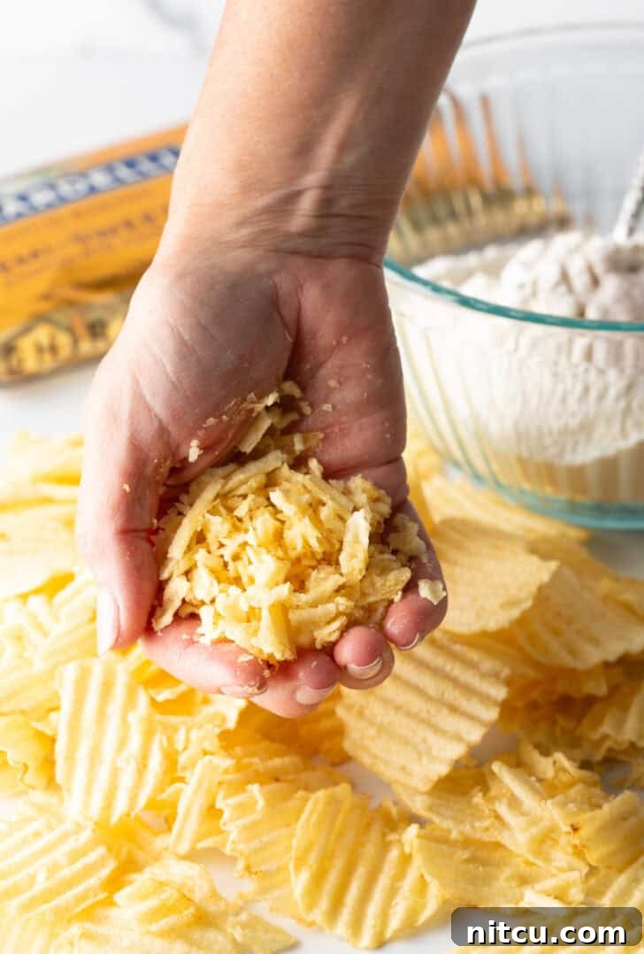 A hand crushing potato chips into smaller pieces.