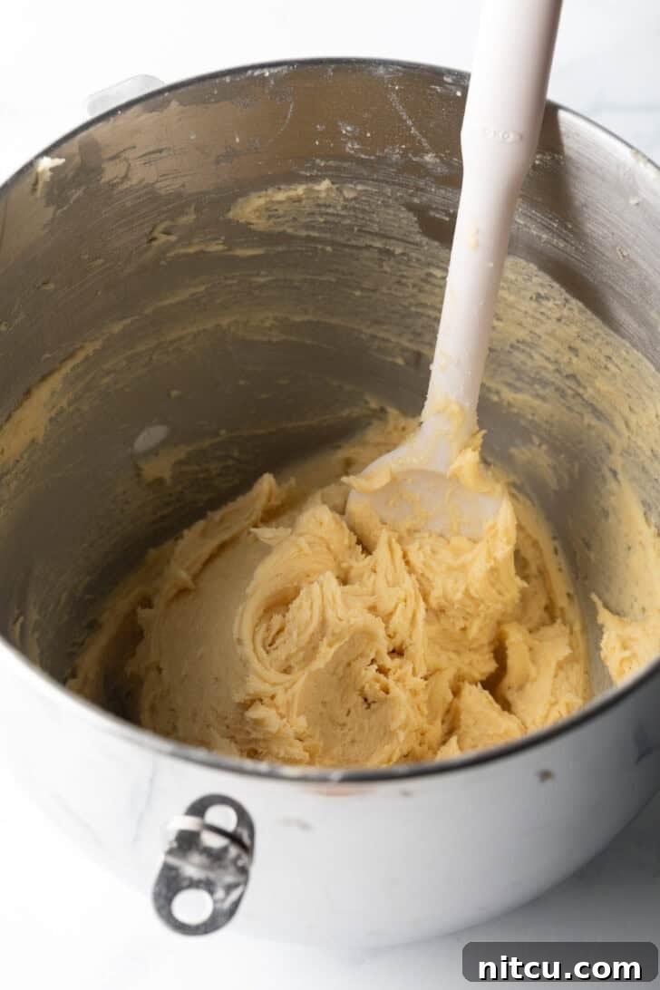 Cookie dough batter being stirred in a metal bowl with a white spoon.