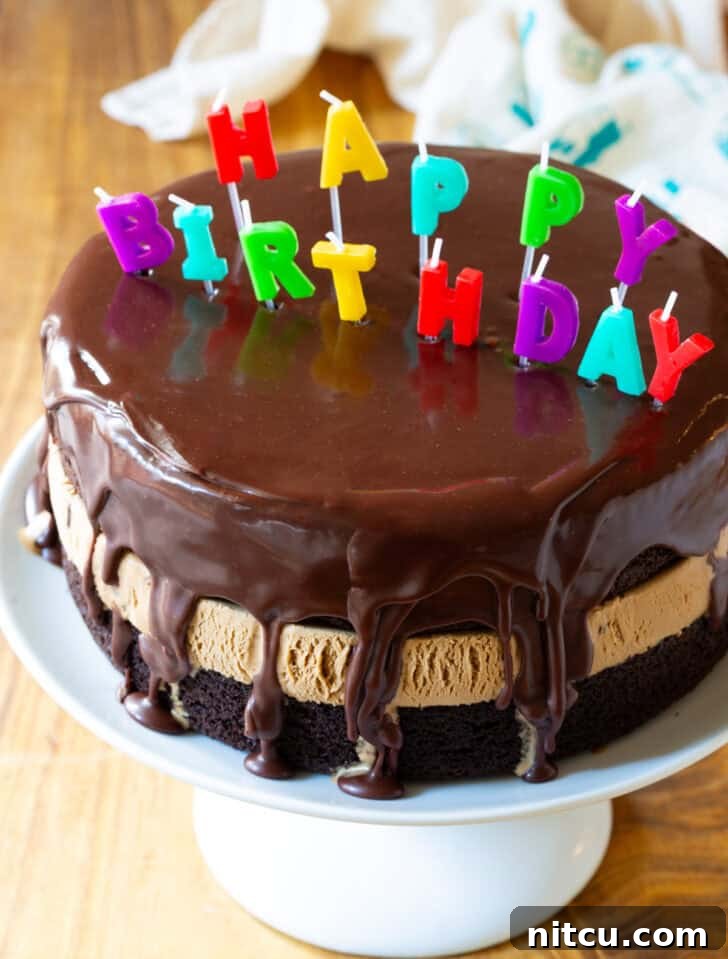 Chocolate and caramel ice cream layered cream cake coated with glossy icing and Happy Birthday candles on top.