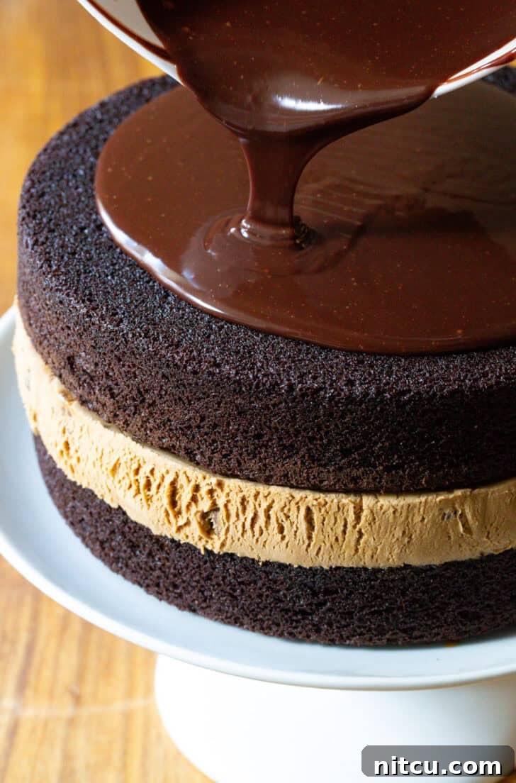 Pouring melted fudge frosting overtop a chocolate and caramel layered ice cream cake.