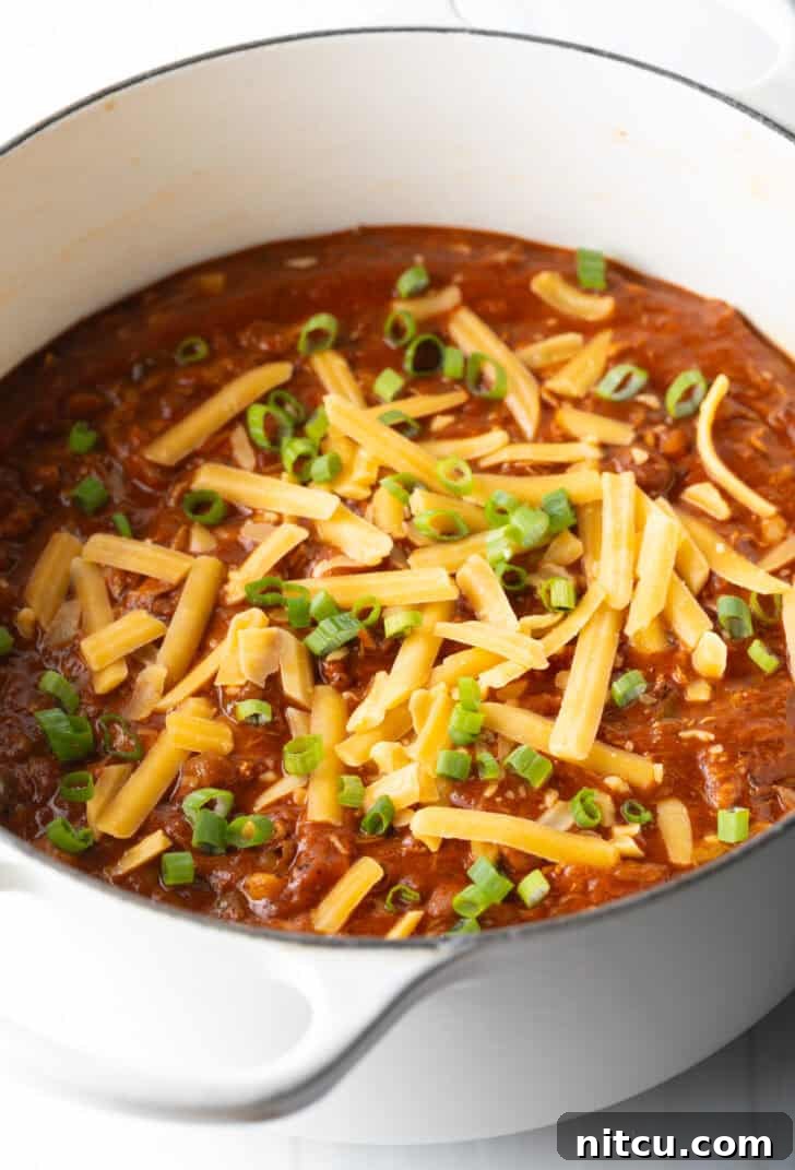 A large, inviting white soup pot filled with the finished chicken chili, beautifully topped with fresh chopped green onions and a generous sprinkle of shredded cheddar cheese, showcasing its vibrant appeal.